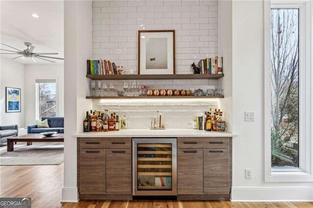 bar featuring tasteful backsplash, ceiling fan, wine cooler, a dry bar, and wood finished floors