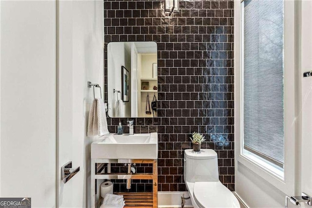 bathroom with a sink, toilet, and tile walls