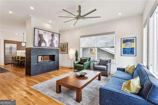 living room featuring a multi sided fireplace, plenty of natural light, recessed lighting, and light wood-style floors