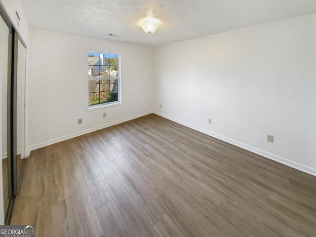 unfurnished bedroom featuring dark wood-type flooring, visible vents, baseboards, and a textured ceiling