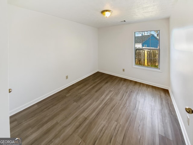 empty room with dark wood-type flooring, visible vents, baseboards, and a textured ceiling