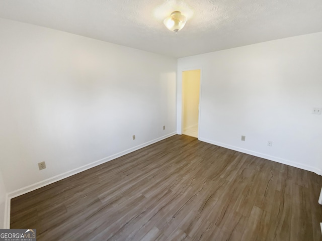 spare room with a textured ceiling, dark wood-type flooring, and baseboards