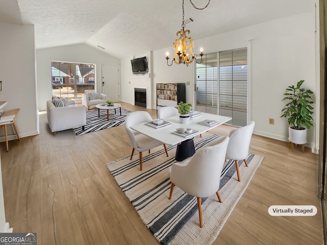 dining space with a notable chandelier, a fireplace, light wood-type flooring, and vaulted ceiling