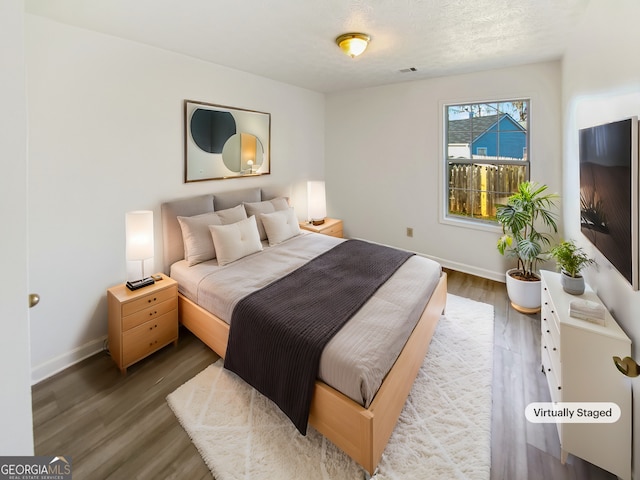 bedroom featuring visible vents, baseboards, a textured ceiling, and wood finished floors