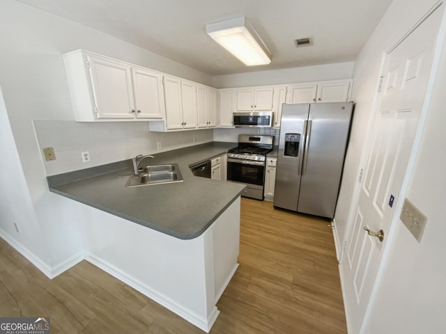 kitchen with wood finished floors, visible vents, a peninsula, a sink, and appliances with stainless steel finishes