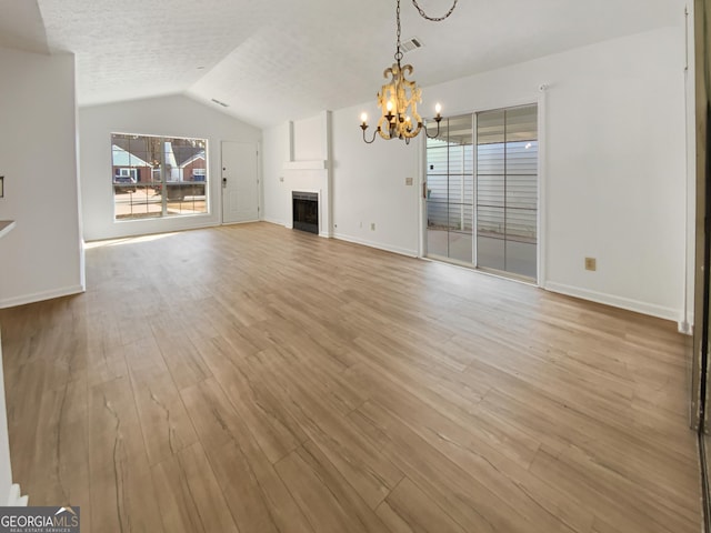 unfurnished living room with wood finished floors, baseboards, an inviting chandelier, a fireplace, and vaulted ceiling