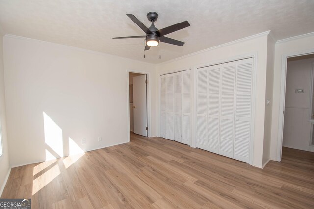 unfurnished bedroom featuring ceiling fan, two closets, light wood-style floors, and ornamental molding