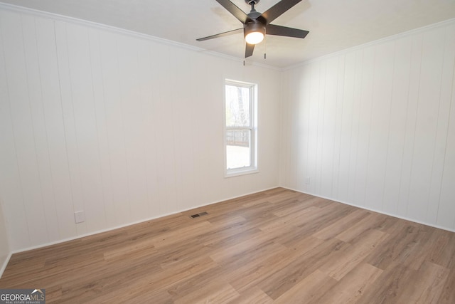 empty room with light wood-style flooring, a ceiling fan, visible vents, and ornamental molding