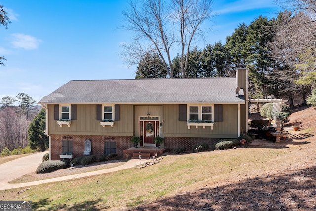 split foyer home with concrete driveway, a front yard, a shingled roof, brick siding, and a chimney