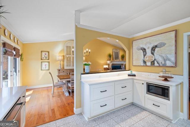 kitchen with stainless steel microwave, ornamental molding, light countertops, and white cabinetry