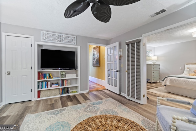 bedroom featuring visible vents, a textured ceiling, wood finished floors, baseboards, and ceiling fan