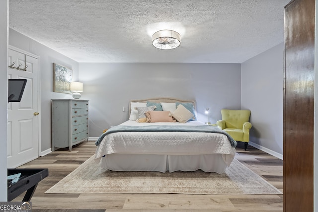 bedroom with wood finished floors, baseboards, and a textured ceiling