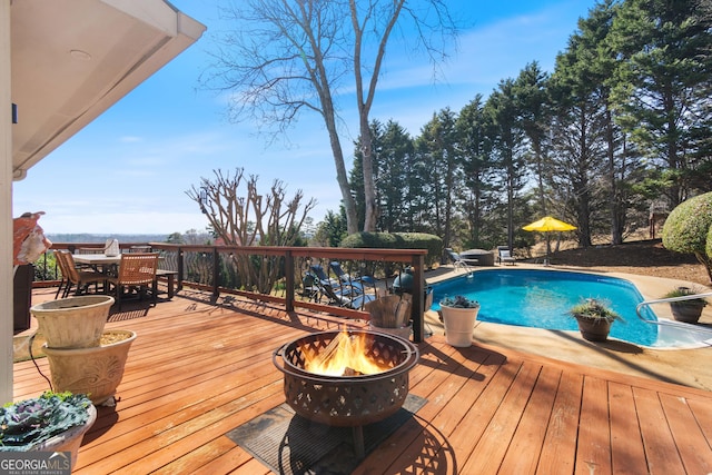 outdoor pool with a fire pit, outdoor dining area, and a deck