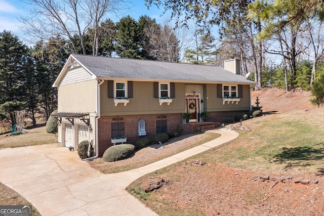 split foyer home with an attached garage, a chimney, concrete driveway, a front lawn, and brick siding