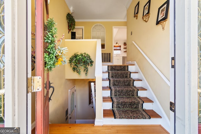 stairs with baseboards, wood finished floors, visible vents, and ornamental molding