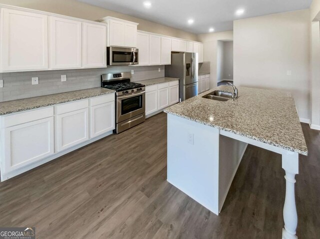 7644 Watson Cir, Locust Grove, GA 30248 - kitchen featuring appliances with stainless steel finishes, dark wood-style floors, a kitchen island with sink, white cabinets, and backsplash