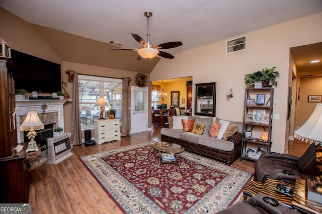 living room featuring visible vents, a tiled fireplace, vaulted ceiling, ceiling fan with notable chandelier, and wood finished floors