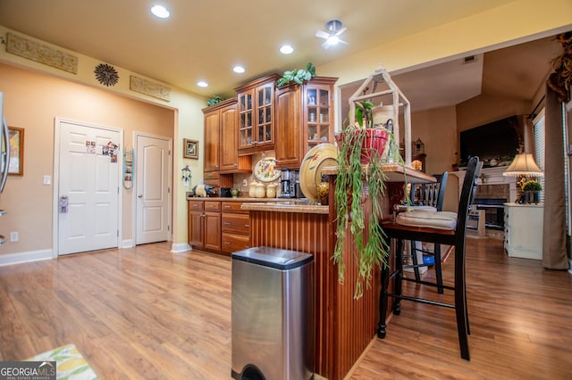 kitchen with brown cabinetry, light wood finished floors, a breakfast bar, and glass insert cabinets