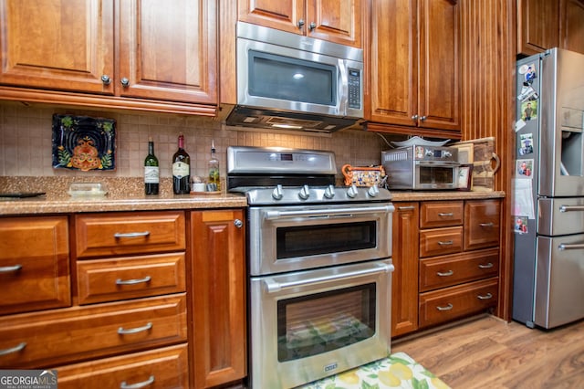 kitchen with brown cabinetry, tasteful backsplash, appliances with stainless steel finishes, and light wood-type flooring