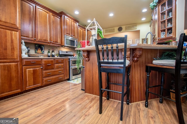 kitchen featuring a breakfast bar, light wood-style flooring, brown cabinets, and appliances with stainless steel finishes