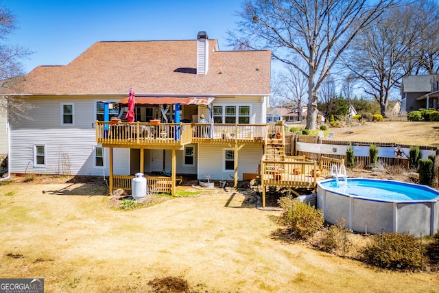 back of property featuring a wooden deck, stairs, a lawn, a chimney, and an outdoor pool