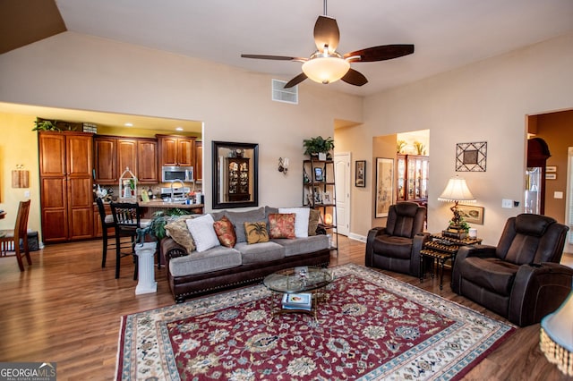 living area with visible vents, ceiling fan, lofted ceiling, and wood finished floors