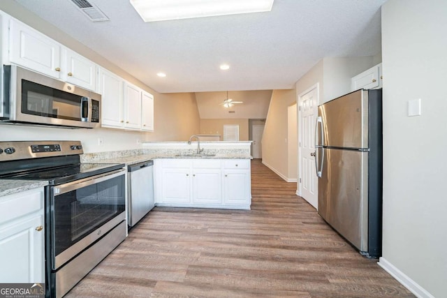 kitchen featuring visible vents, a peninsula, a sink, appliances with stainless steel finishes, and white cabinetry