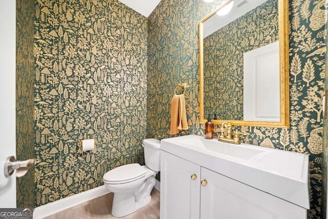 half bath featuring wallpapered walls, toilet, vanity, and wood finished floors