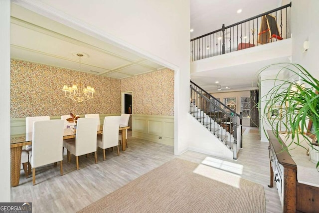 unfurnished dining area with a wainscoted wall, wood finished floors, stairway, wallpapered walls, and a chandelier