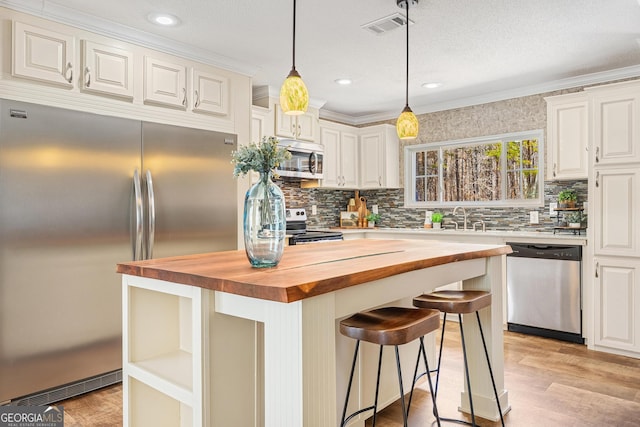 kitchen with white cabinetry, ornamental molding, appliances with stainless steel finishes, and butcher block countertops