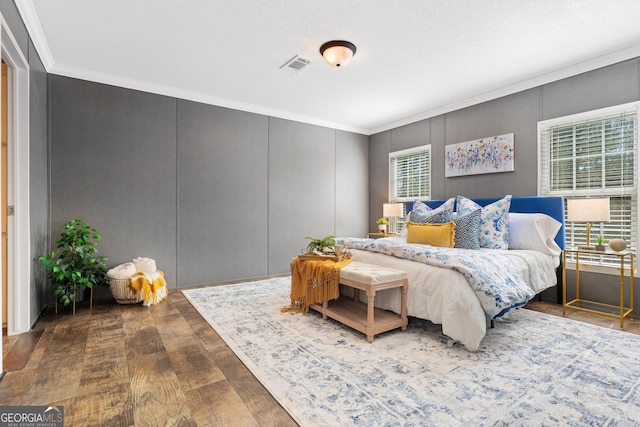 bedroom featuring visible vents, wood finished floors, crown molding, and a decorative wall