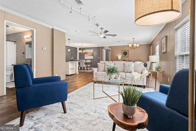 living area with visible vents, wood finished floors, crown molding, and ceiling fan with notable chandelier