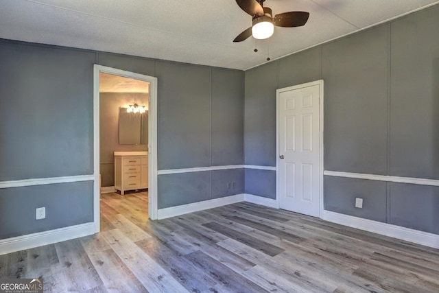 unfurnished bedroom with a ceiling fan, a decorative wall, wood finished floors, and baseboards