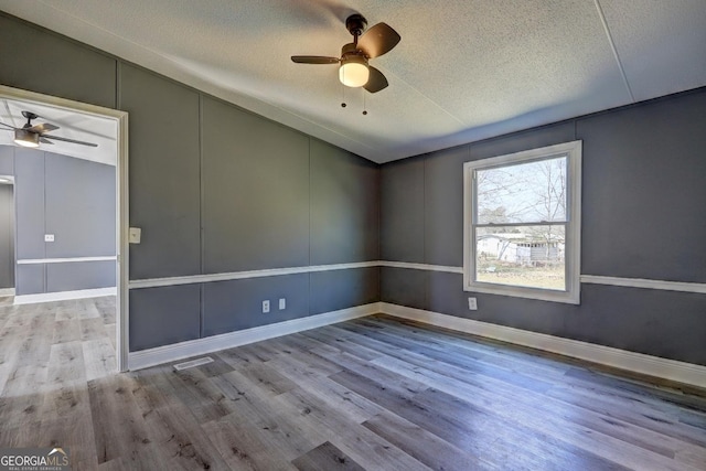 empty room featuring ceiling fan, lofted ceiling, wood finished floors, and a textured ceiling