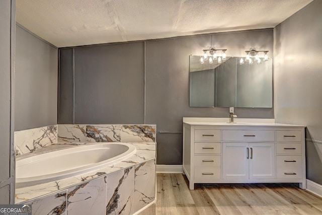 bathroom with a garden tub, a textured ceiling, wood finished floors, baseboards, and vanity