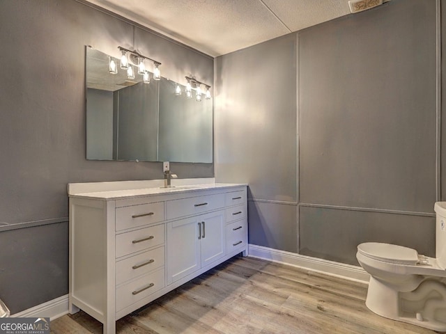 bathroom with baseboards, toilet, vanity, wood finished floors, and a textured ceiling