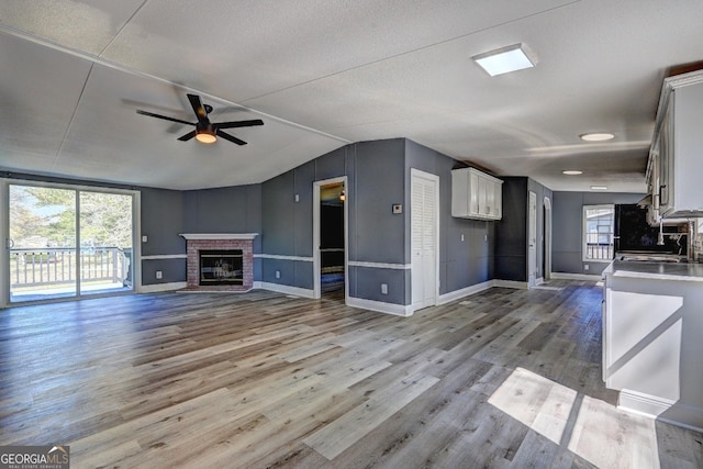 unfurnished living room with a wealth of natural light, a brick fireplace, wood finished floors, and ceiling fan