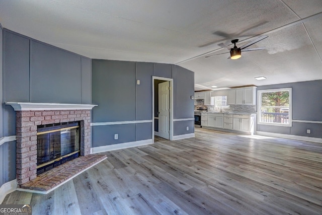 unfurnished living room featuring baseboards, lofted ceiling, light wood-style flooring, ceiling fan, and a brick fireplace