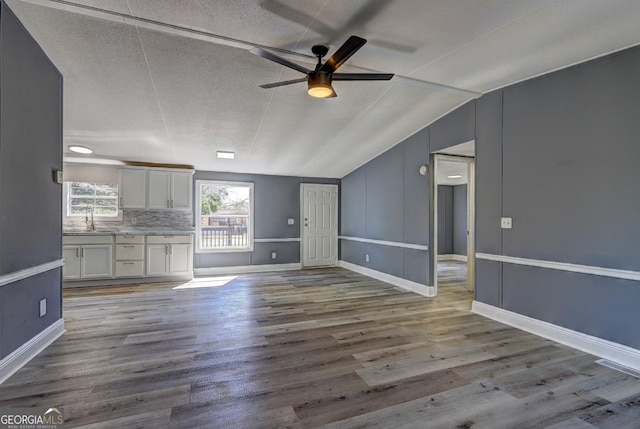 unfurnished living room featuring wood finished floors, baseboards, visible vents, lofted ceiling, and a sink