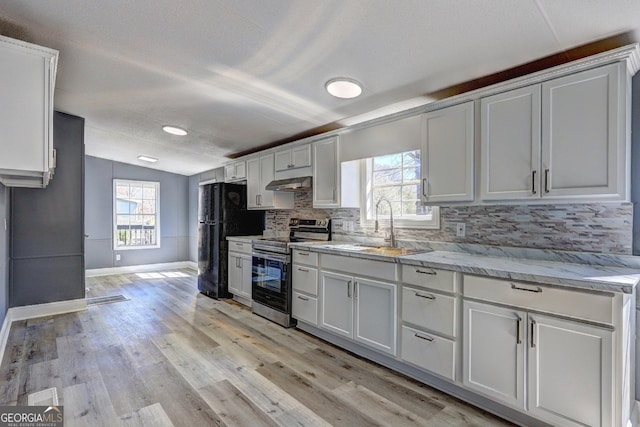 kitchen featuring tasteful backsplash, under cabinet range hood, vaulted ceiling, stainless steel range with electric cooktop, and freestanding refrigerator