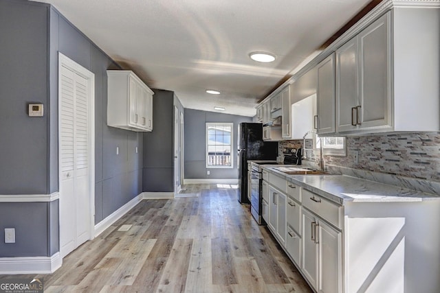 kitchen featuring baseboards, a sink, decorative backsplash, stainless steel range with electric cooktop, and light wood-type flooring