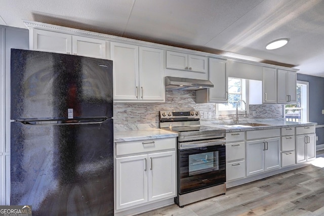 kitchen featuring backsplash, range hood, freestanding refrigerator, electric range, and a sink