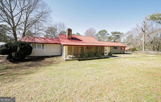 back of property featuring a yard, metal roof, a chimney, and fence