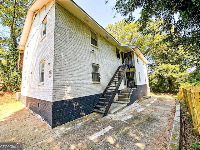 exterior space featuring brick siding, stairway, crawl space, and fence