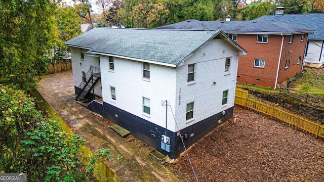 exterior space featuring brick siding, a shingled roof, stairs, and fence