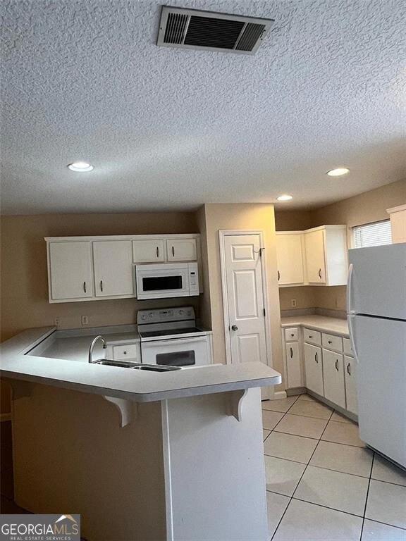 kitchen with visible vents, white cabinetry, white appliances, a peninsula, and light tile patterned floors