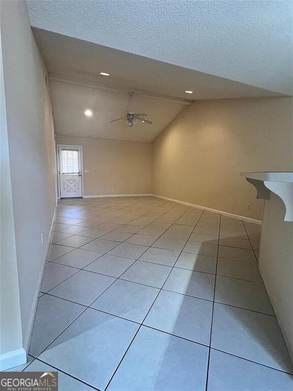 empty room featuring light tile patterned floors, baseboards, a textured ceiling, and ceiling fan