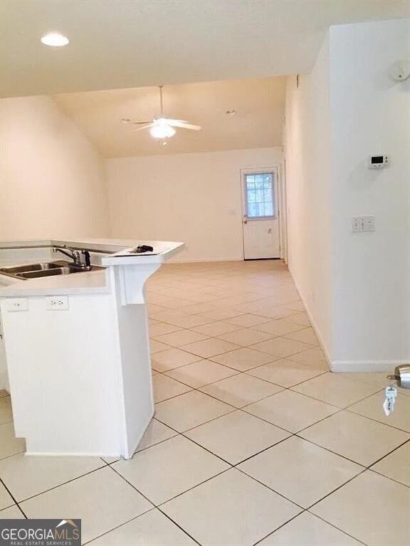 kitchen with light countertops, light tile patterned flooring, white cabinetry, a ceiling fan, and a sink