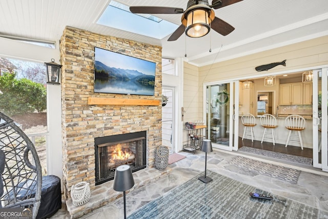 living room with wooden walls, stone finish flooring, a warm lit fireplace, a skylight, and a ceiling fan