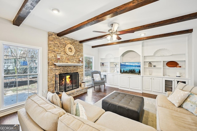 living area featuring beam ceiling, a fireplace, dark wood-type flooring, and ceiling fan